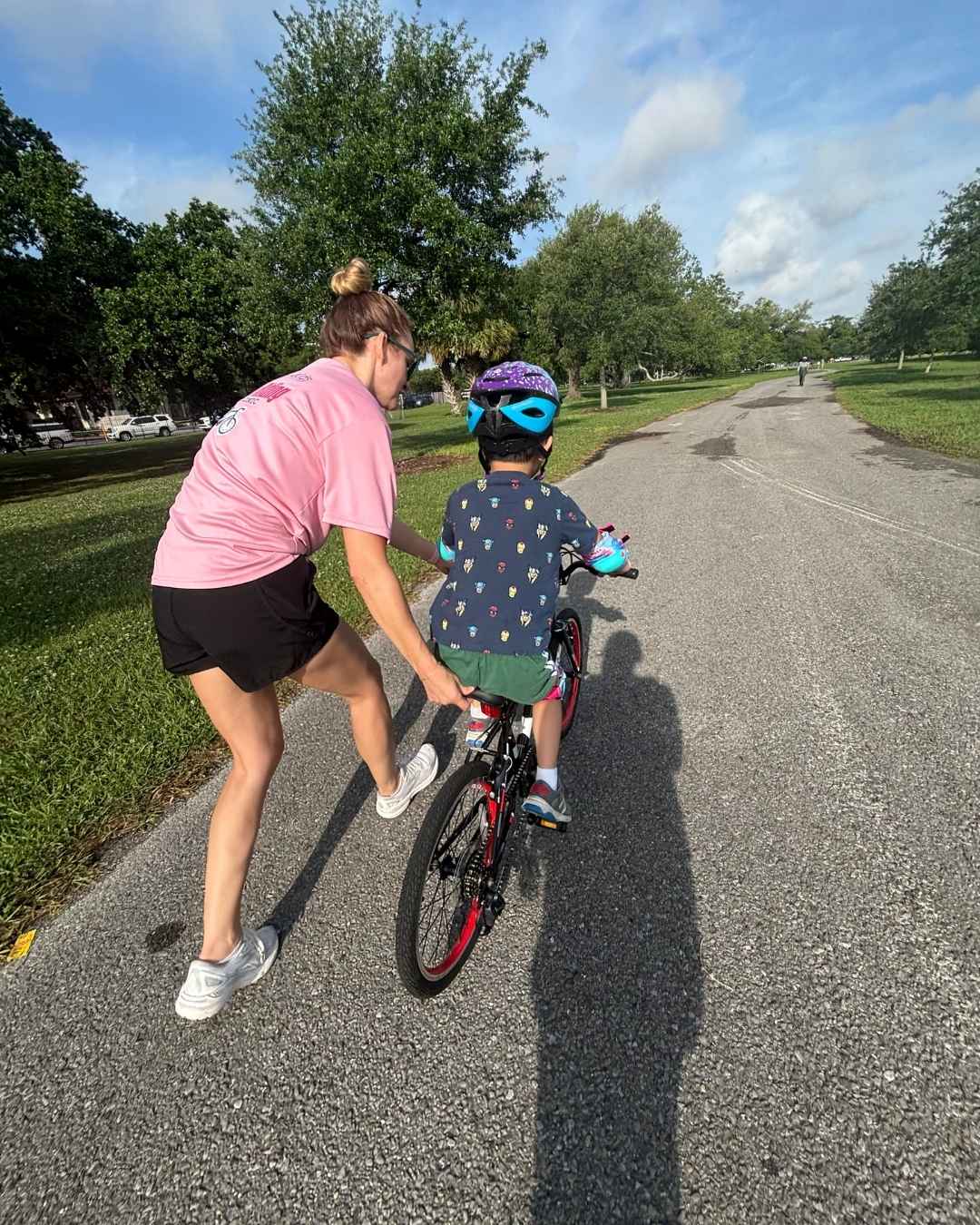 A person pushing a child on a bike down a road
