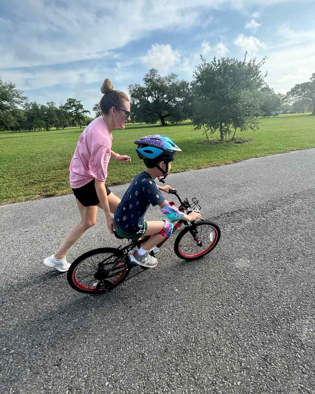 A person pushing a child on a bike in a park